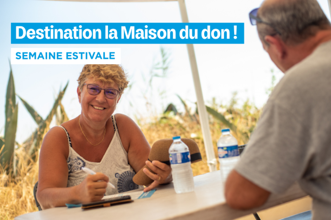 Une femme souriante aux cheveux blonds et portant des lunettes, assise à une table en plein air, elle rempli le questionnaire pré-don. Elle est en conversation avec un homme dont on ne voit que le dos. Le fond montre un champ de blé et un ciel bleu. En haut de l'image, un bandeau bleu affiche le texte « Destination la Maison du don ! » et en dessous, « SEMAINE ESTIVALE ».